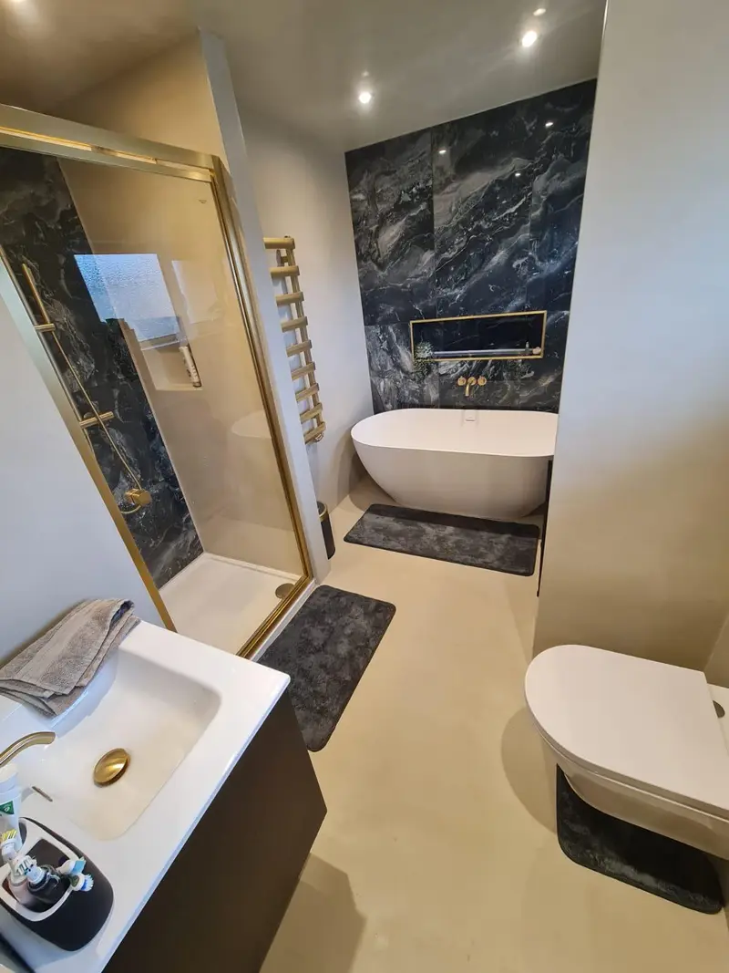 Seamless cream microcement bathroom with freestanding bath and dark marble feature wall
